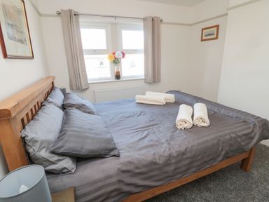A bedroom with a wooden bed with gray bedding and towels on the bed at Bisley House in Amble