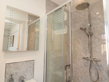 A bathroom with a glass shower enclosure a rain shower head and a mirror on the wall at Bisley House in Amble