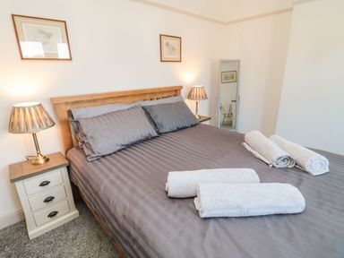 A bedroom with a wooden bed frame grey bedding bedside tables with lamps and rolled towels on the bed at Bisley House in Amble