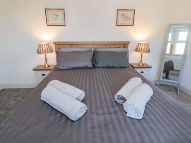 A bedroom with a double bed with striped bedding two bedside tables with lamps a floor mirror and rolled towels on the bed at Bisley House in Amble