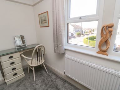 A small desk with a chair and mirror next to a window with a wooden sculpture on the windowsill at Bisley House in Amble