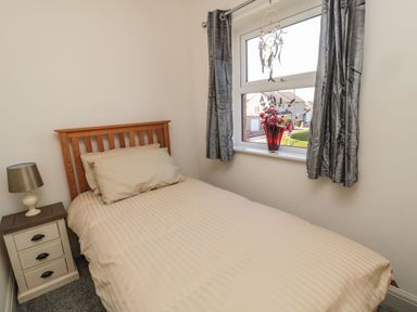 A bedroom with a single bed a bedside table with a lamp a window with curtains and a flower vase at Bisley House in Amble