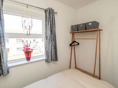 A bedroom with a window a red vase with flowers a dreamcatcher grey curtains a wooden clothes rack and a bed at Bisley House in Amble
