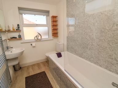 A bathroom with a bathtub shower toilet sink window and shelves at Bisley House in Amble