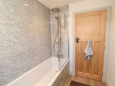 A bathroom with a bathtub shower with a glass screen and a wooden door with a towel hanging at Bisley House in Amble