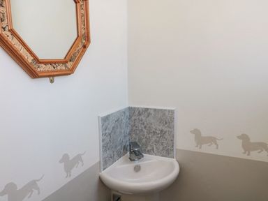 A corner sink with a faucet below a decorative mirror and wall decals of small dog silhouettes at Bisley House in Amble