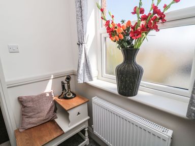 A corner with a wooden bench with cushion and vintage telephone next to a window with a vase of flowers at Bisley House in Amble