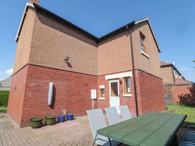 An outdoor patio area with a green table and chairs next to a brick and pebble dash house at Bisley House in Amble