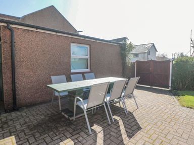 An outdoor patio area with a table and six chairs next to a building and wooden gate at Bisley House in Amble