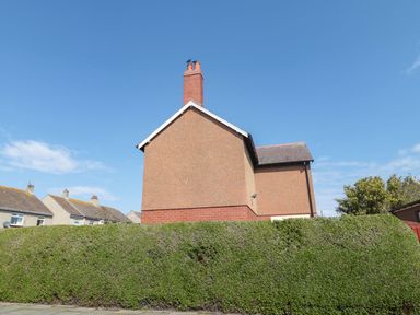 Side view of a two-story house with a chimney and a tall hedge in front at Bisley House in Amble