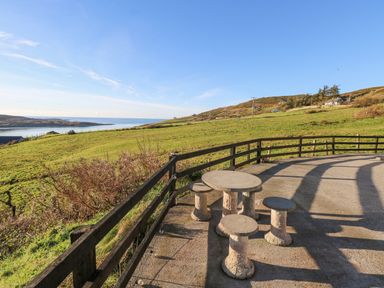 A patio area with a round stone table and stools overlooking green fields and water at Castle Demesne House in Clifden County Galway