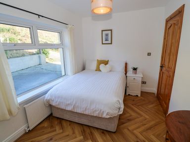 A bedroom with a bed next to a window a nightstand with a plant a wooden door and parquet flooring at Castle Demesne House Clifden County Galway