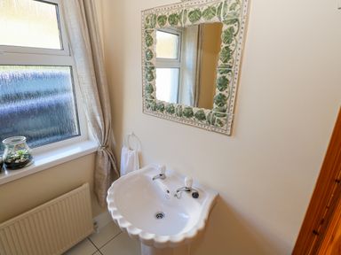 A bathroom with a white sink a decorative mirror a window with a curtain and a white towel on a holder at Castle Demesne House in Clifden County Galway