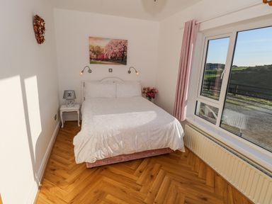 A bedroom with a double bed bedside table lamp wall lights painting window and pink curtains at Castle Demesne House in Clifden County Galway
