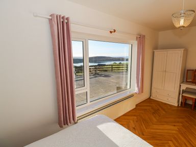 A bedroom with pink curtains a white wardrobe a small desk a chair and a window showing an outdoor view at Castle Demesne House in Clifden County Galway