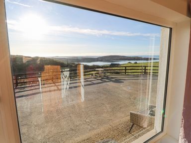 A window view showing an outdoor patio with a stone table and benches overlooking grassy hills and water at Castle Demesne House in Clifden County Galway