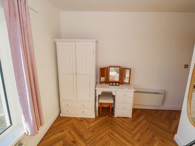 A corner of a room with a white wardrobe and a white vanity table with a wooden framed mirror and a chair at Castle Demesne House in Clifden County Galway