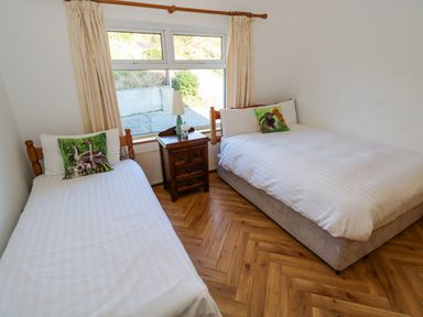 A bedroom with two single beds a wooden nightstand and a window with beige curtains at Castle Demesne House in Clifden County Galway
