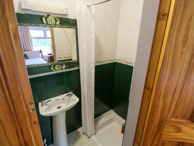 A bathroom with a pedestal sink shower area and a mirror reflecting a bedroom at Castle Demesne House in Clifden County Galway