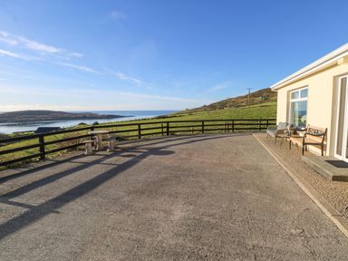 A concrete patio with outdoor seating and a small stone table overlooking grassy hills and a body of water at Castle Demesne House in Clifden County Galway