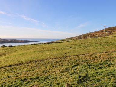 A grassy field with hills and telephone poles overlooking the sea at Castle Demesne House in Clifden County Galway