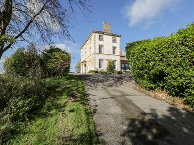 A three story house with windows at the end of a driveway with bushes and trees at Rockstowes House Uley near Dursley