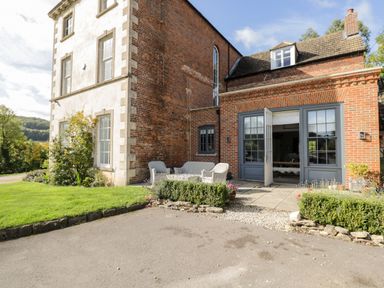 A patio with outdoor seating and open double doors leading into a brick house at Rockstowes House Uley near Dursley