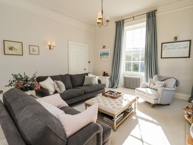 A living room with two dark sofas a white armchair a tufted ottoman and blue curtains at Rockstowes House Uley near Dursley