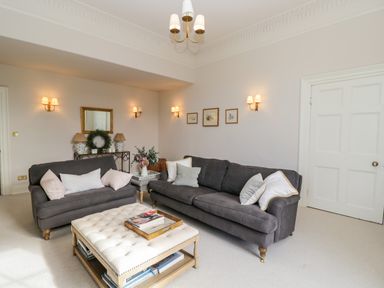 A living room with two dark sofas a cushioned ottoman coffee table and wall lights at Rockstowes House Uley near Dursley