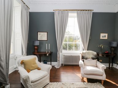 A sitting room with two armchairs and side tables by windows at Rockstowes House Uley near Dursley