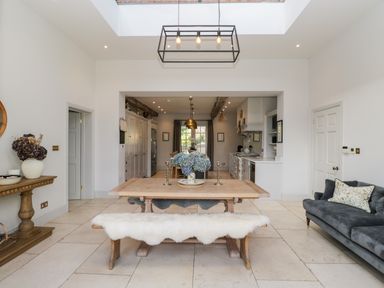 A dining area with a wooden table and bench next to a kitchen and a gray sofa at Rockstowes House in Uley near Dursley