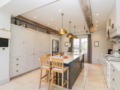 A kitchen with an island, wooden chairs, hanging brass pendant lights, large cabinets, and double doors at Rockstowes House Uley near Dursley