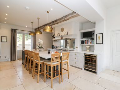 A kitchen with a large island and wooden chairs under brass pendant lights at Rockstowes House in Uley near Dursley