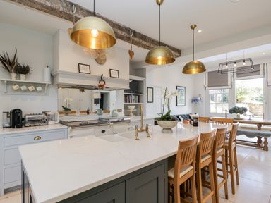 A kitchen with a large island and wooden chairs under hanging pendant lights at Rockstowes House in Uley near Dursley