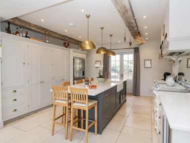 A kitchen with a central island and wooden stools under pendant lights at Rockstowes House in Uley near Dursley