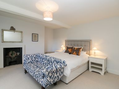 A bedroom with a double bed, two bedside tables and lamps, a patterned blue and white sofa, a fireplace, and a wall mirror at Rockstowes House in Uley near Dursley