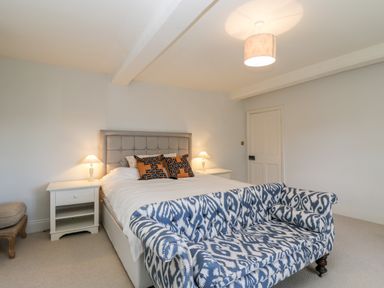 A bedroom with a bed flanked by bedside tables with lamps and a patterned sofa at the foot of the bed at Rockstowes House in Uley near Dursley