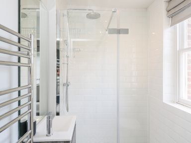 A bathroom with a shower area a glass shower screen a towel rack and a sink under a mirror at Rockstowes House in Uley near Dursley