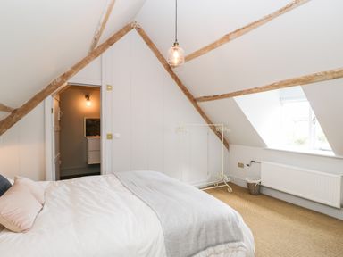 A bedroom with a bed a window a small white clothes rack and wooden beams on the ceiling at Rockstowes House in Uley near Dursley