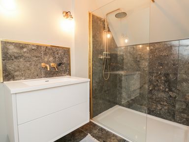 A bathroom with a white sink cabinet gold faucets a walk in shower with dark stone tiles at Rockstowes House in Uley near Dursley