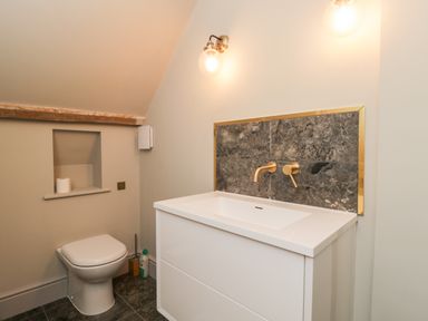 A bathroom with a toilet a white sink with gold fixtures and gray tiled floor at Rockstowes House Uley near Dursley