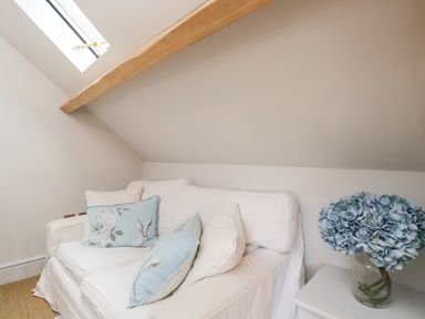 A white sofa with blue floral cushions under a sloped ceiling near a skylight window and a vase of blue flowers on a white side table at Rockstowes House in Uley near Dursley