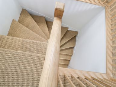 A spiral staircase with carpeted steps and wooden handrail at Rockstowes House in Uley near Dursley