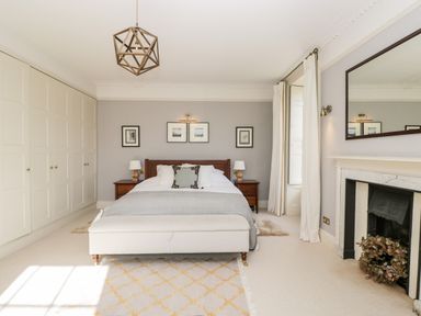 A bedroom with a bed and bedside tables built in wardrobes and a fireplace at Rockstowes House in Uley near Dursley