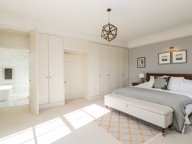 A bedroom with a bed a bench at the foot of the bed built in wardrobes and an open door leading to a bathroom at Rockstowes House in Uley near Dursley