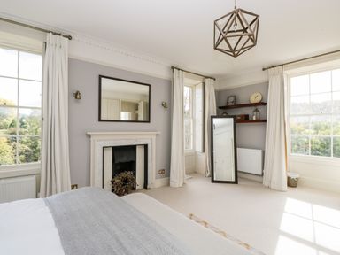 A bedroom with a bed a fireplace a standing mirror and shelves with decor at Rockstowes House Uley near Dursley