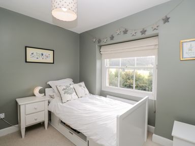 A bedroom with a white bed and side table with window and star decorations at Rockstowes House in Uley near Dursley