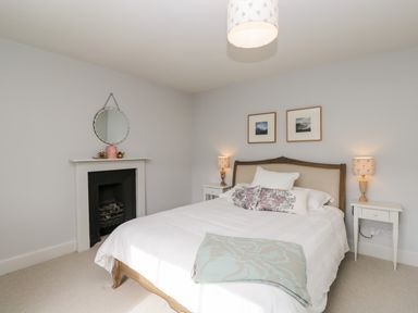 A bedroom with a double bed two nightstands with lamps a fireplace and a round mirror at Rockstowes House Uley near Dursley