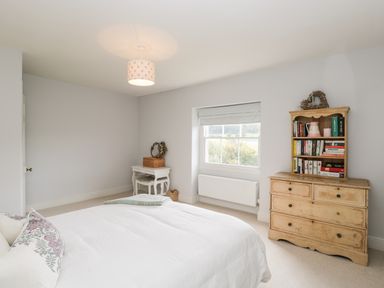 A bedroom with a bed a wooden dresser with books and a small desk by the window at Rockstowes House Uley near Dursley