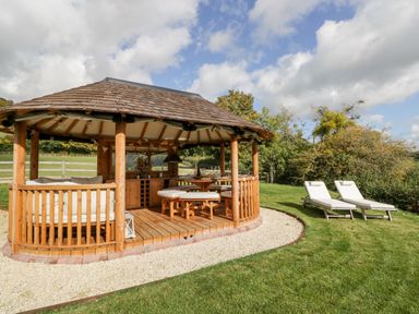 A wooden gazebo with seating and a table on a lawn with two sun loungers at Rockstowes House Uley near Dursley